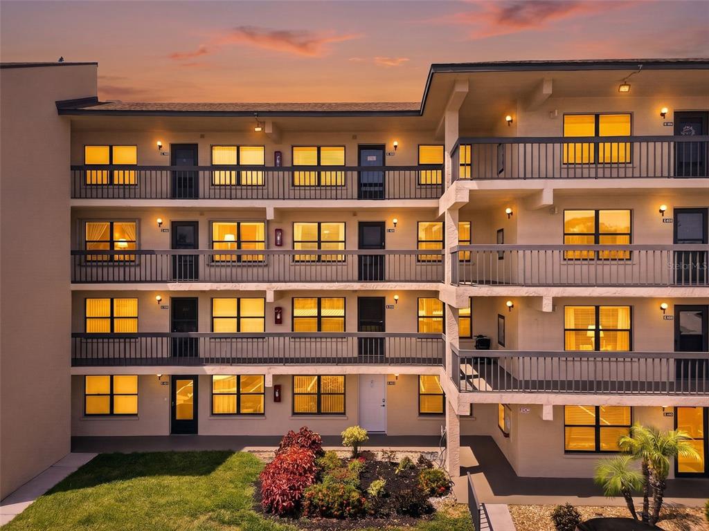 An exterior view of a multi-story apartment building with balconies and illuminated windows at dusk — 505 30TH AVENUE W UNIT E303, BRADENTON, FL