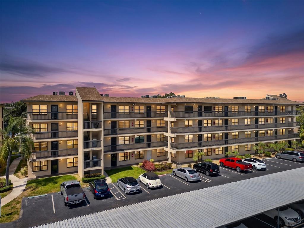 A multi-story apartment building with exterior balconies and a parking lot at sunset — 505 30TH AVENUE W UNIT E303, BRADENTON, FL