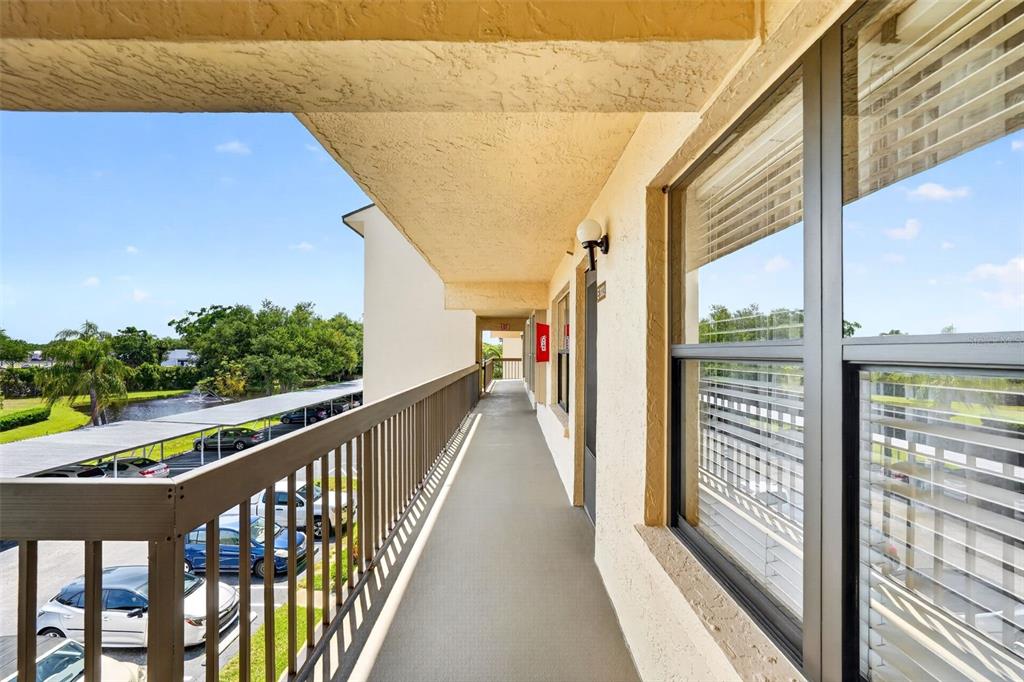An outdoor apartment walkway features a metal railing overlooking a parking lot and pond — 505 30TH AVENUE W UNIT E303, BRADENTON, FL
