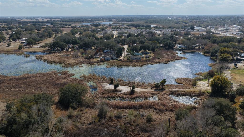 An aerial view shows a lake surrounded by trees, marshy vegetation, and nearby residential houses — 800 US HIGHWAY 17 92 S, DAVENPORT, FL