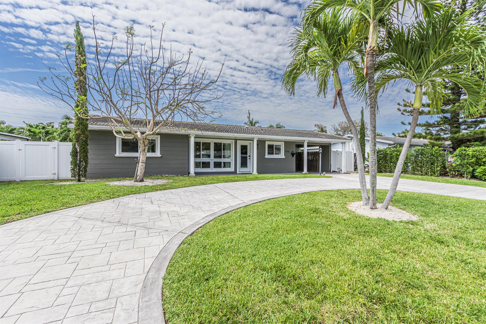 A gray single-story house features a curved stamped concrete driveway and palm trees — 2770 NE 53rd Street, Lighthouse Point FL 33064, LIGHTHOUSE POINT, FL