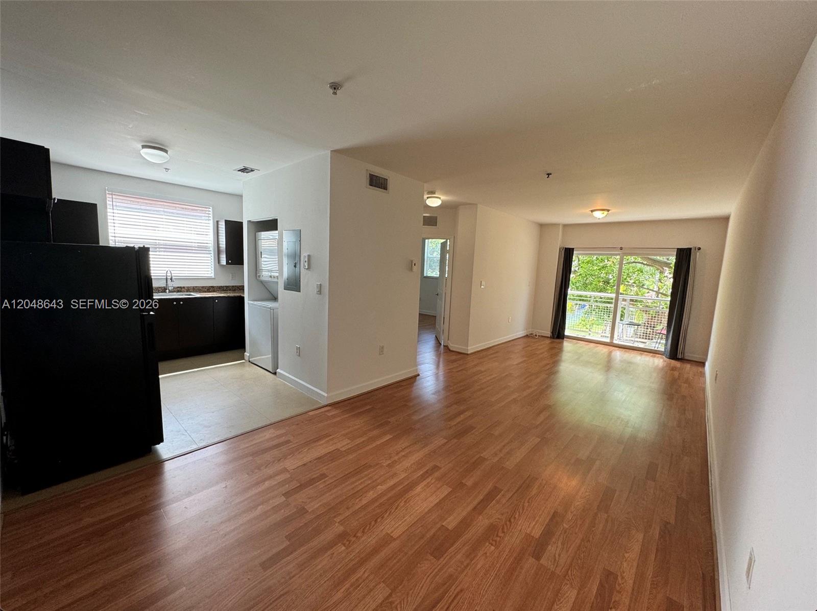 An open-concept living area features wood-look flooring, a kitchen with dark cabinets, and a balcony — 529 NE 62nd St # 203, Miami FL 33138, MIAMI, FL