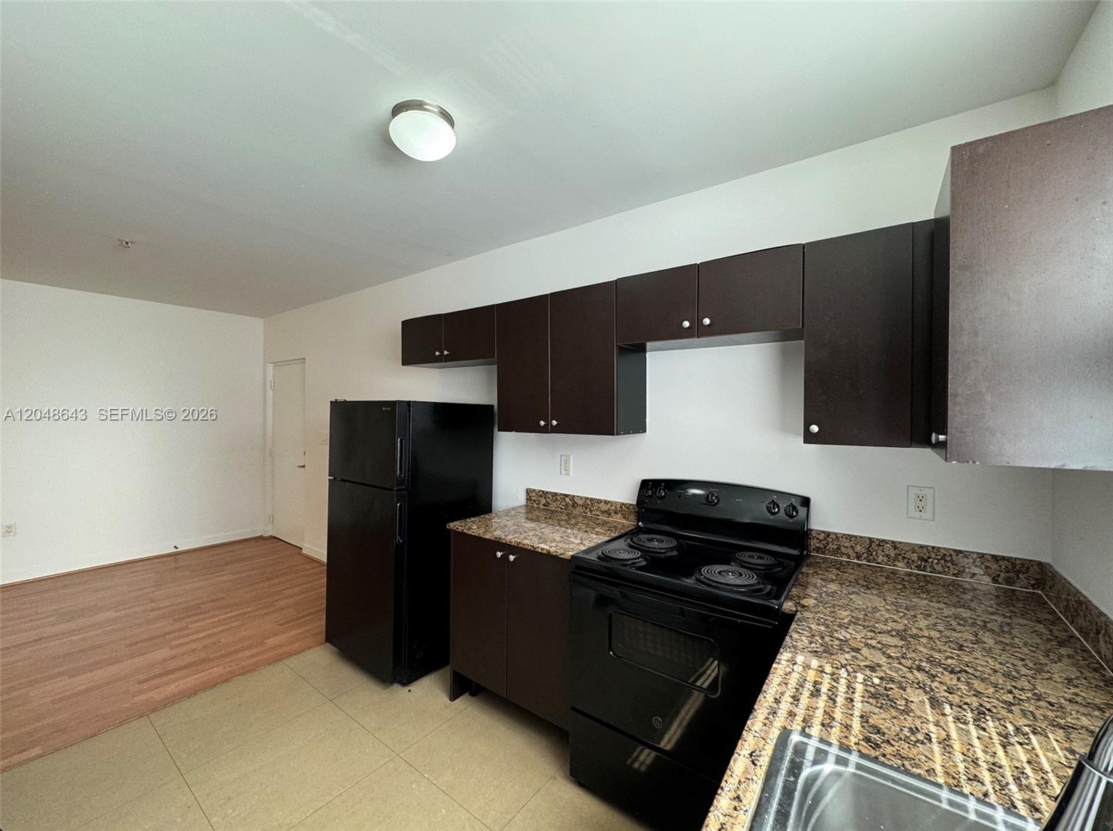 A kitchen features dark brown cabinets, black appliances, and granite countertops over tile flooring — 529 NE 62nd St # 203, Miami FL 33138, MIAMI, FL