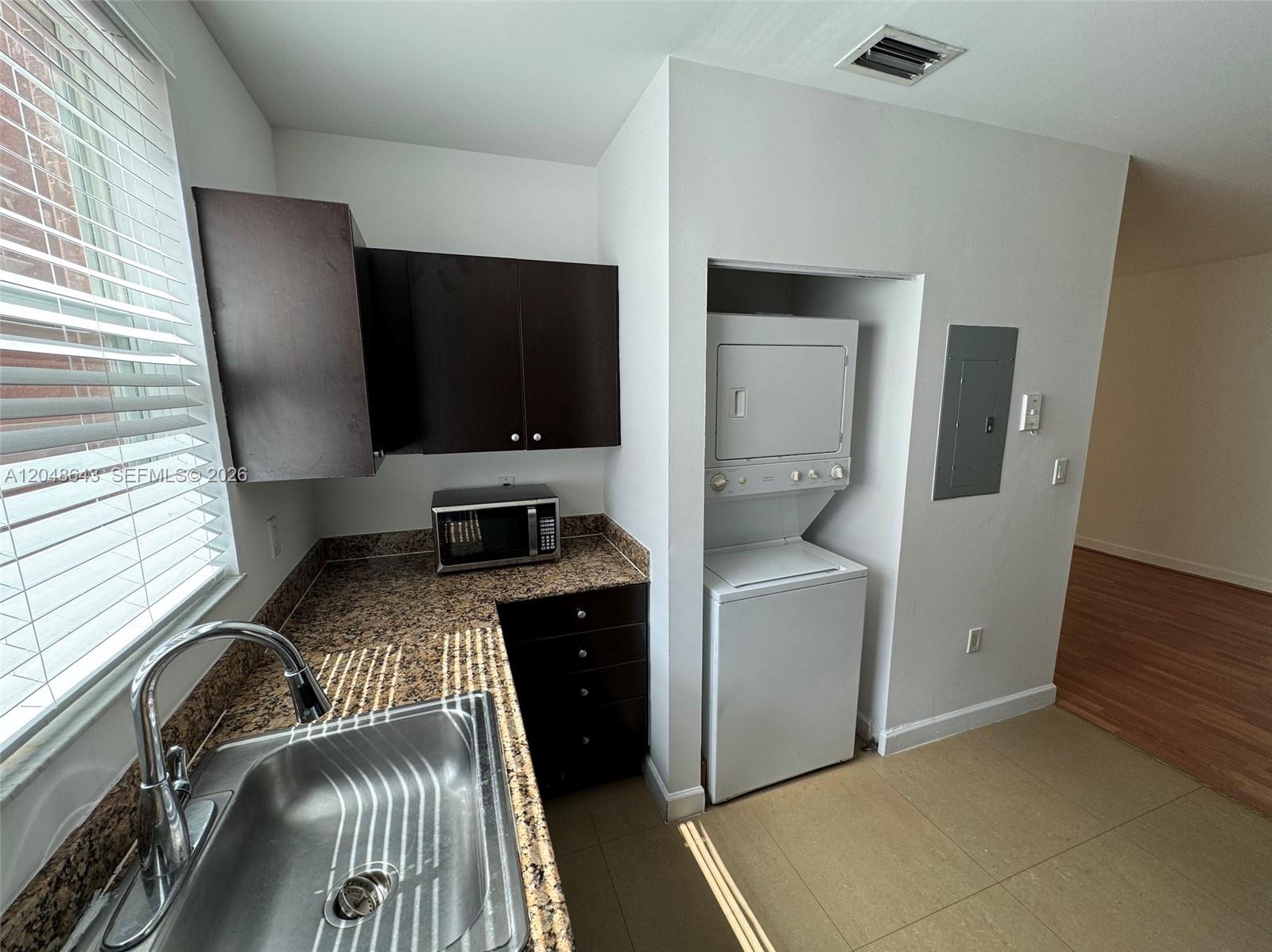 A kitchen features dark cabinets, granite countertops, a stainless steel sink, and a stacked washer-dryer — 529 NE 62nd St # 203, Miami FL 33138, MIAMI, FL