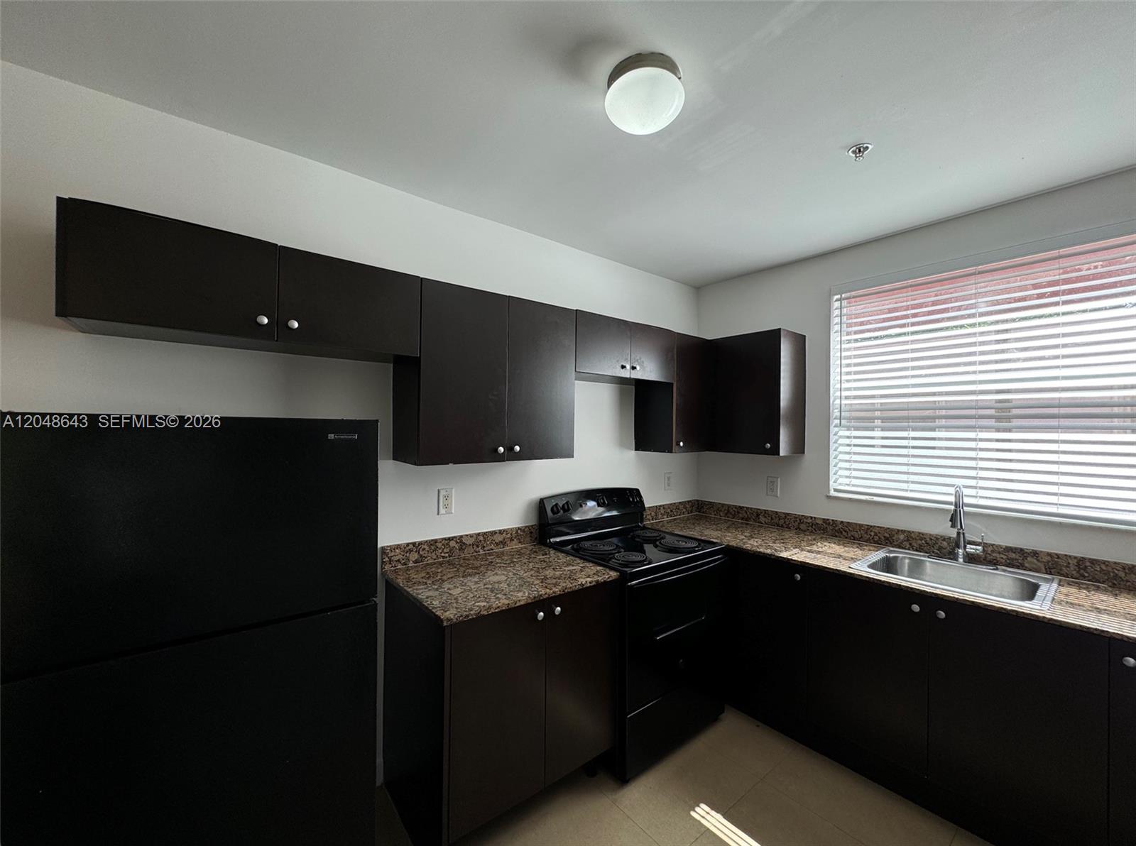 A kitchen features dark brown cabinets, granite countertops, black appliances, and a window above the sink — 529 NE 62nd St # 203, Miami FL 33138, MIAMI, FL