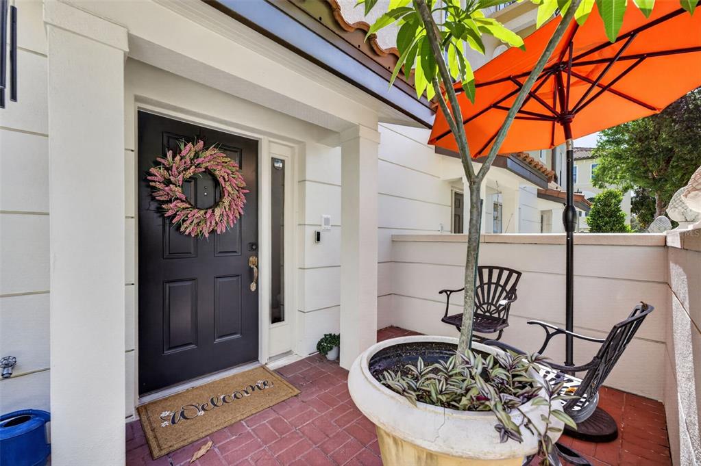 A black front door with a floral wreath opens onto a brick patio with seating — 4908 SAN MARINO CIRCLE, LAKE MARY, FL