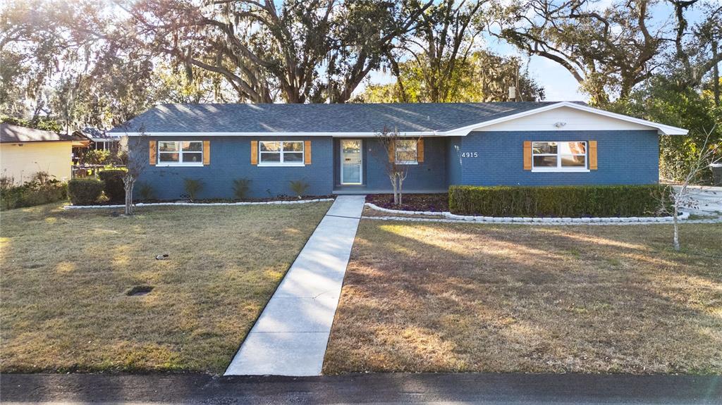 A single-story blue brick house features a gray shingled roof and a concrete walkway — 4915 WHITEOAK DRIVE E, LAKELAND, FL
