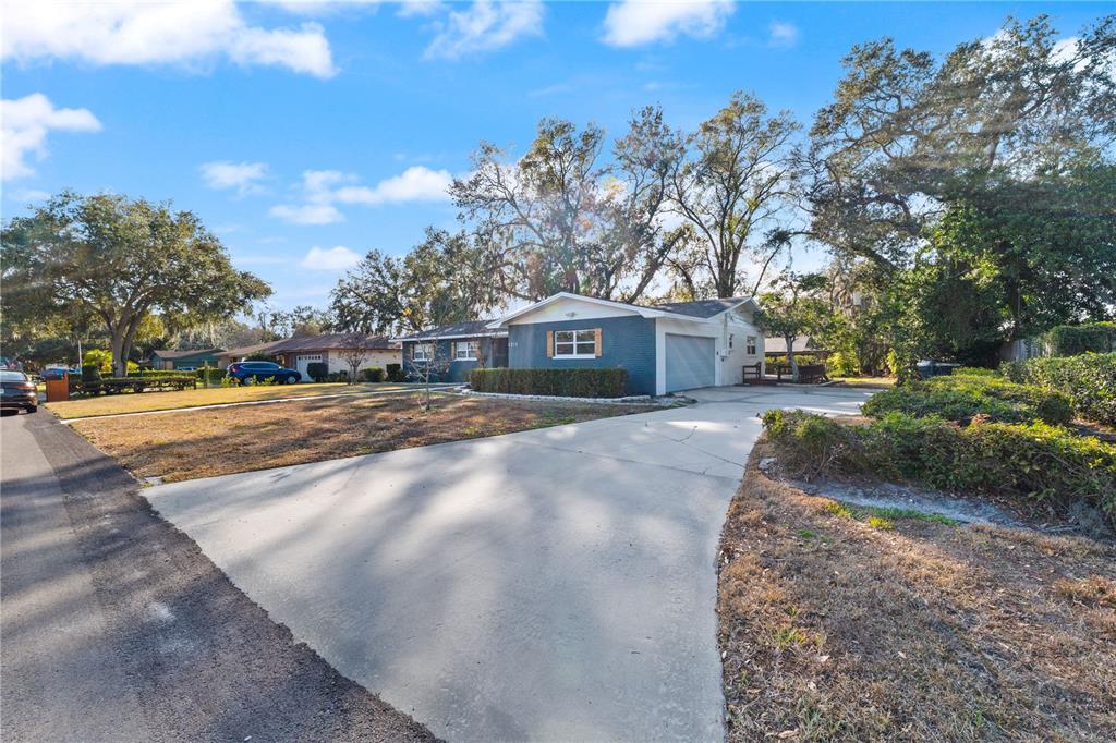 A single-story blue brick house with a concrete driveway and mature trees in the yard — 4915 WHITEOAK DRIVE E, LAKELAND, FL