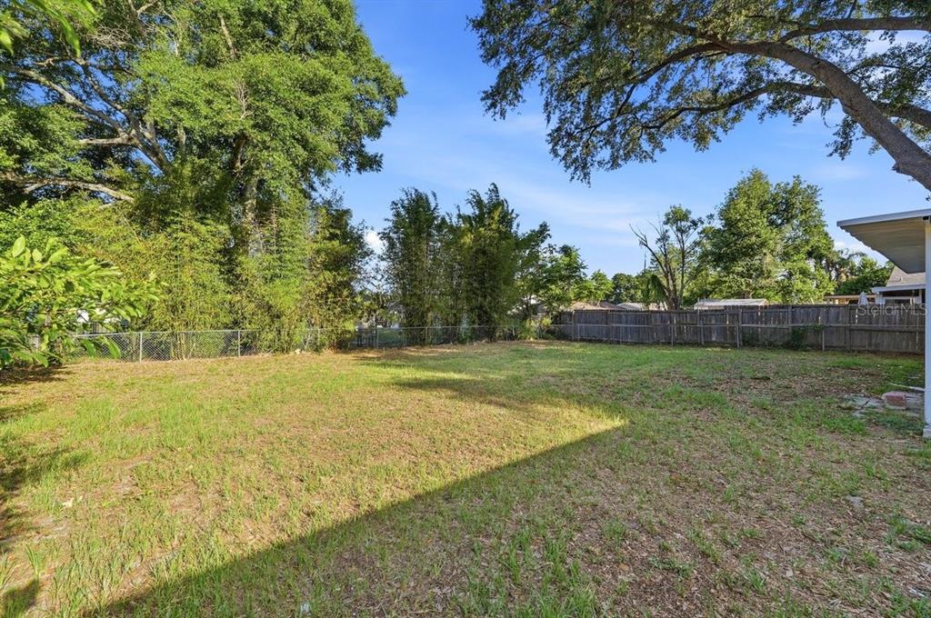 A grassy backyard features a chain-link fence, a wooden privacy fence, and mature trees — 137 LOWELL ROAD, WINTER HAVEN, FL