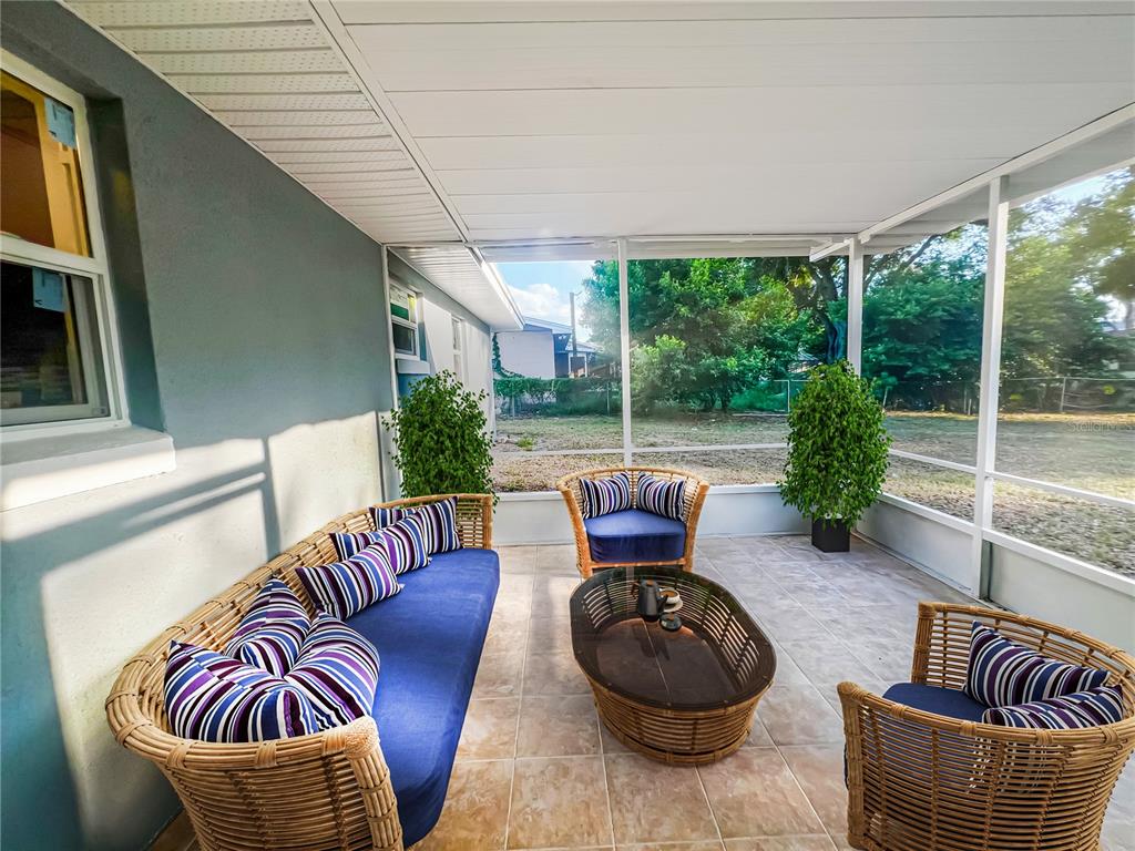 A screened-in patio features wicker furniture with blue and purple striped cushions on tile flooring — 137 LOWELL ROAD, WINTER HAVEN, FL