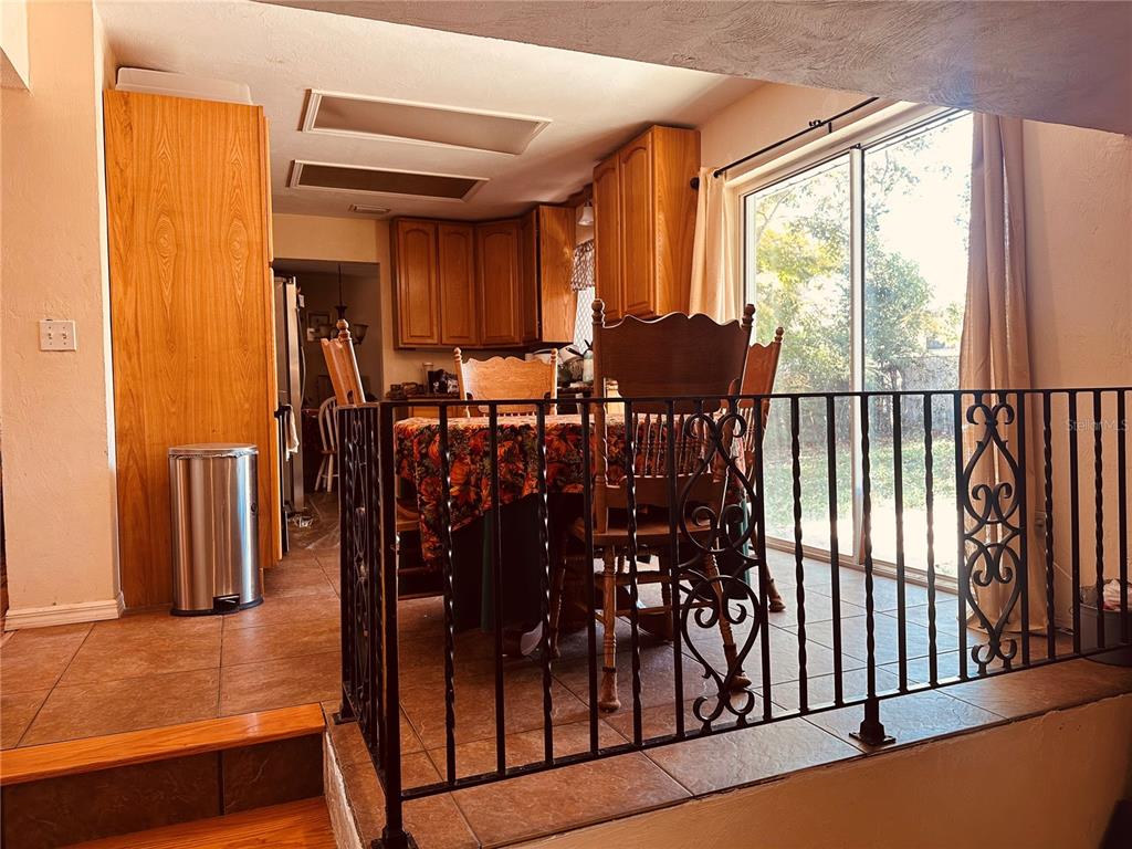 A dining area with wood cabinets, tile flooring, and a decorative black metal railing — 1649 E SHANGRI LA DRIVE, DAYTONA BEACH, FL