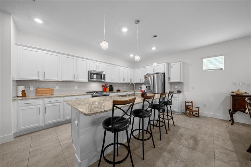 A kitchen features white cabinets, granite countertops, a central island with bar seating, and tile flooring — 4378 NW 54TH TERRACE, OCALA, FL