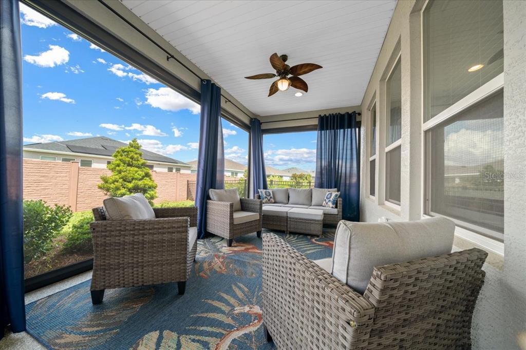 A covered patio features wicker furniture, a ceiling fan, and blue curtains overlooking a backyard — 4378 NW 54TH TERRACE, OCALA, FL