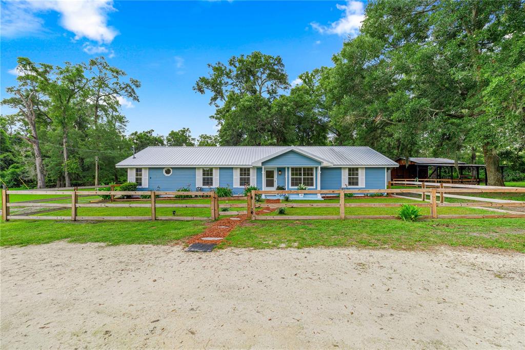 A blue single-story house with a metal roof sits behind a wooden split-rail fence — 1890 NW 167TH PLACE, TRENTON, FL