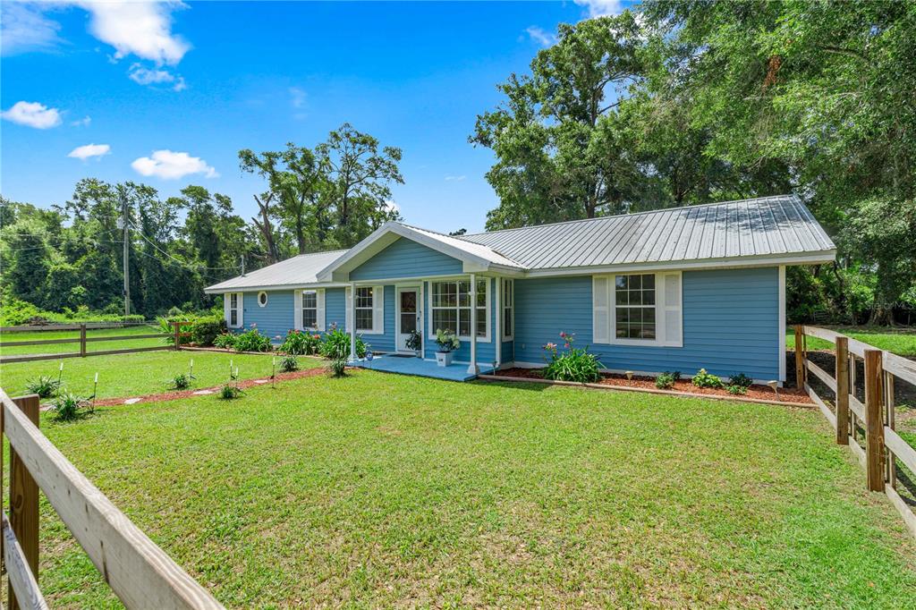 A blue single-story house with a metal roof sits behind a wooden fence — 1890 NW 167TH PLACE, TRENTON, FL