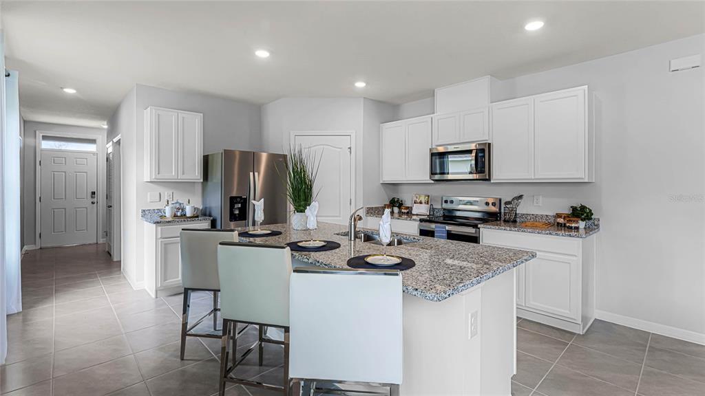A kitchen features white cabinets, granite countertops, a central island with seating, and tile flooring — 7080 FLINT CREEK DRIVE, LAND O LAKES, FL