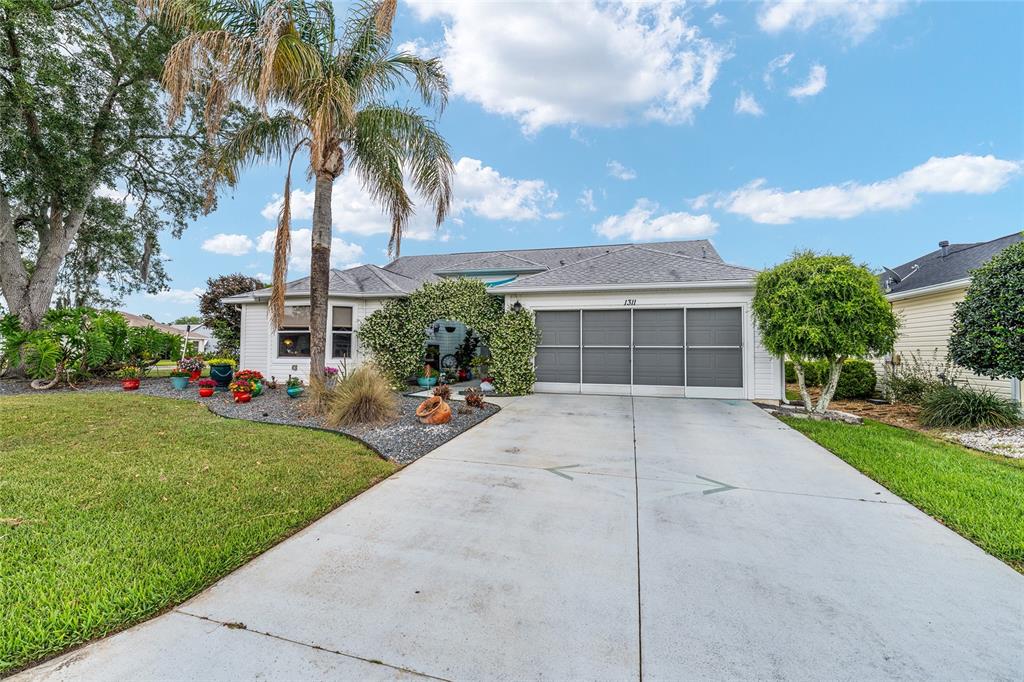 A single-story house with a white exterior, a gray garage door, and a palm tree — 1311 OPORTO DRIVE, THE VILLAGES, FL