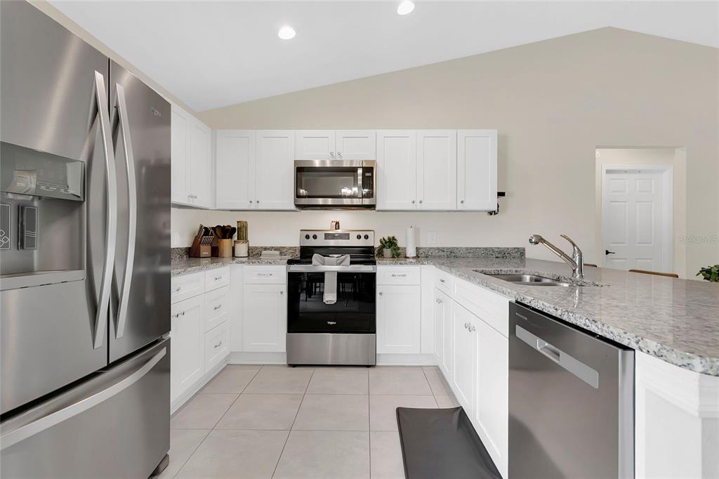 A kitchen features white cabinets, stainless steel appliances, and granite countertops with tile flooring — 1725 NE 160TH PLACE, CITRA, FL
