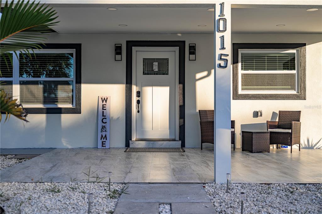 A white front door with a welcome sign sits on a tiled porch with seating — 1015 BOCA CIEGA ISLE DRIVE, ST PETE BEACH, FL