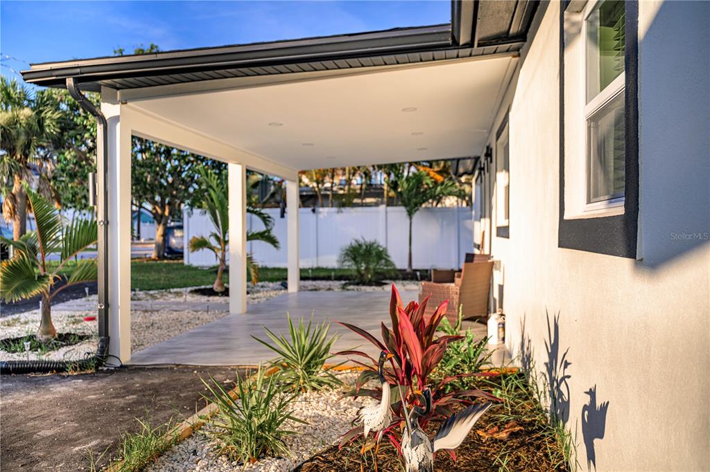 A covered patio with a light-colored floor sits beside a house with white walls — 1015 BOCA CIEGA ISLE DRIVE, ST PETE BEACH, FL