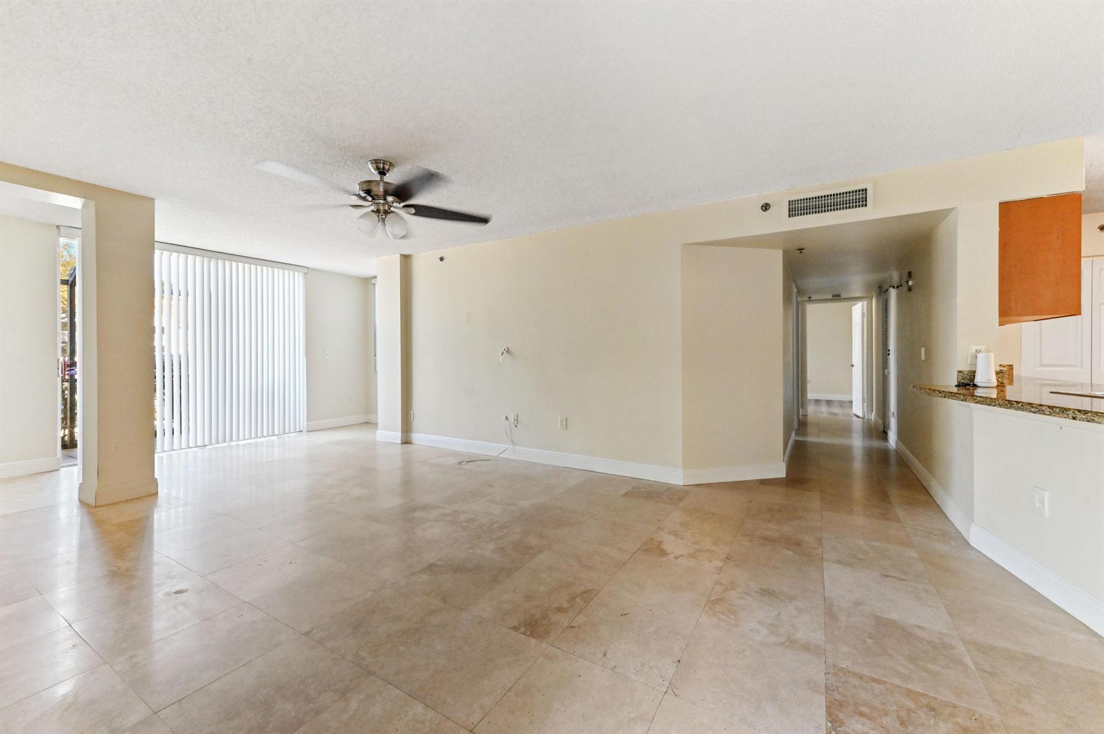 An empty living room features beige tile flooring, a ceiling fan, and a sliding glass door — 3237 Clint Moore Road # 107, Boca Raton FL 33496, BOCA RATON, FL