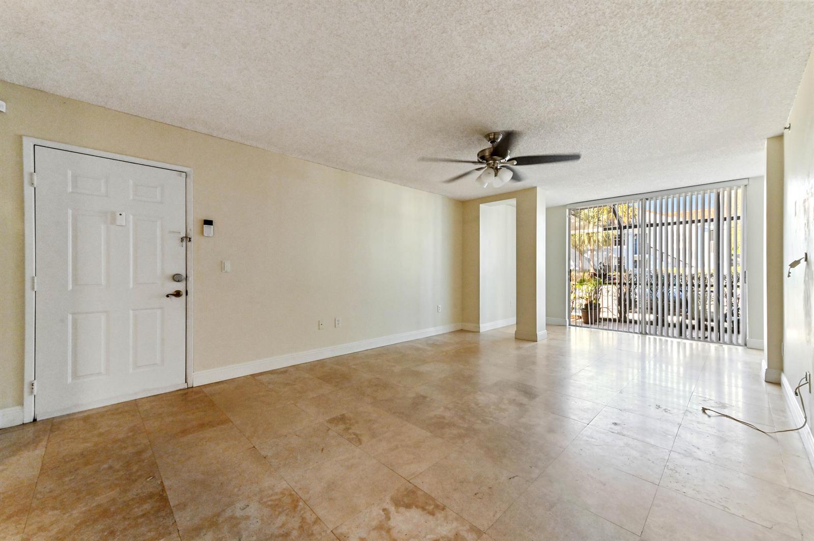 An empty living room features beige tile flooring, a ceiling fan, and sliding glass doors — 3237 Clint Moore Road # 107, Boca Raton FL 33496, BOCA RATON, FL