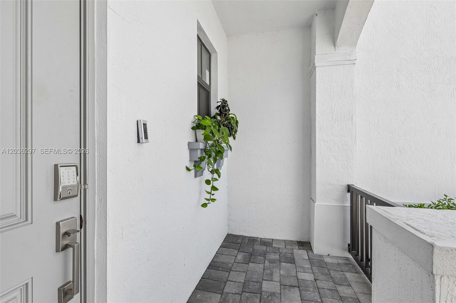 A white exterior entryway features a paved floor, a window with a hanging plant, and a keypad lock — 592 NW 203rd Ter, Miami Gardens FL 33169, MIAMI GARDENS, FL