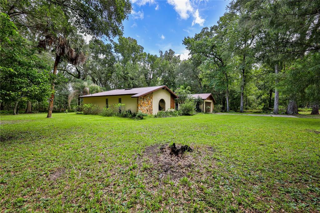A single-story house with stone accents and a metal roof sits on a grassy lot — 18255 LAKE LINDSEY ROAD, BROOKSVILLE, FL