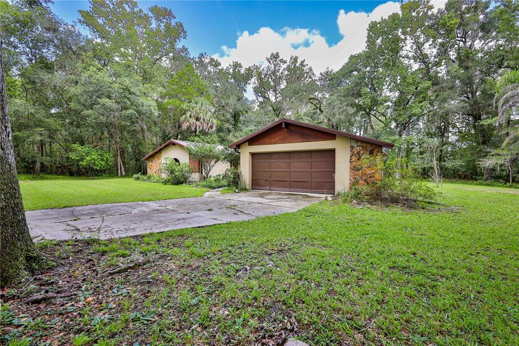 A detached garage with a brown door and stone accents sits on a grassy lot — 18255 LAKE LINDSEY ROAD, BROOKSVILLE, FL