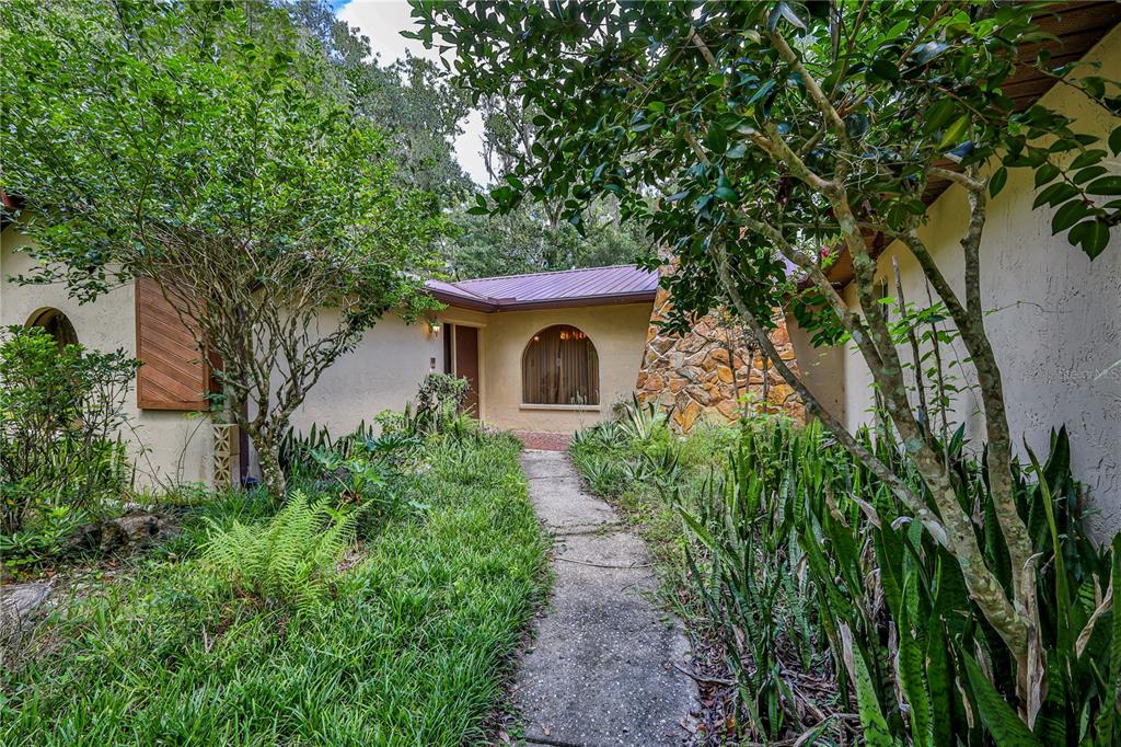 A concrete walkway leads to the entrance of a house with stone accents and landscaping — 18255 LAKE LINDSEY ROAD, BROOKSVILLE, FL