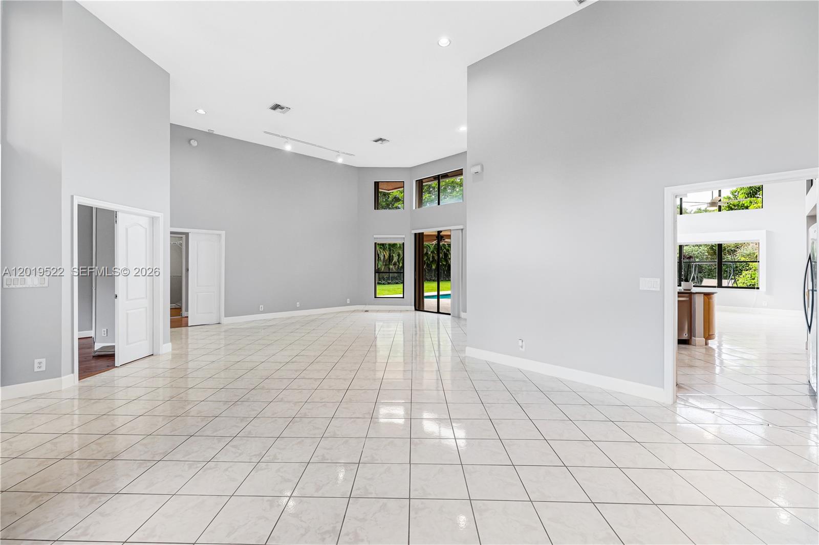 A spacious, empty living room features high ceilings, white tile floors, and large windows — 1256 S Manor Dr S, Weston FL 33326, WESTON, FL