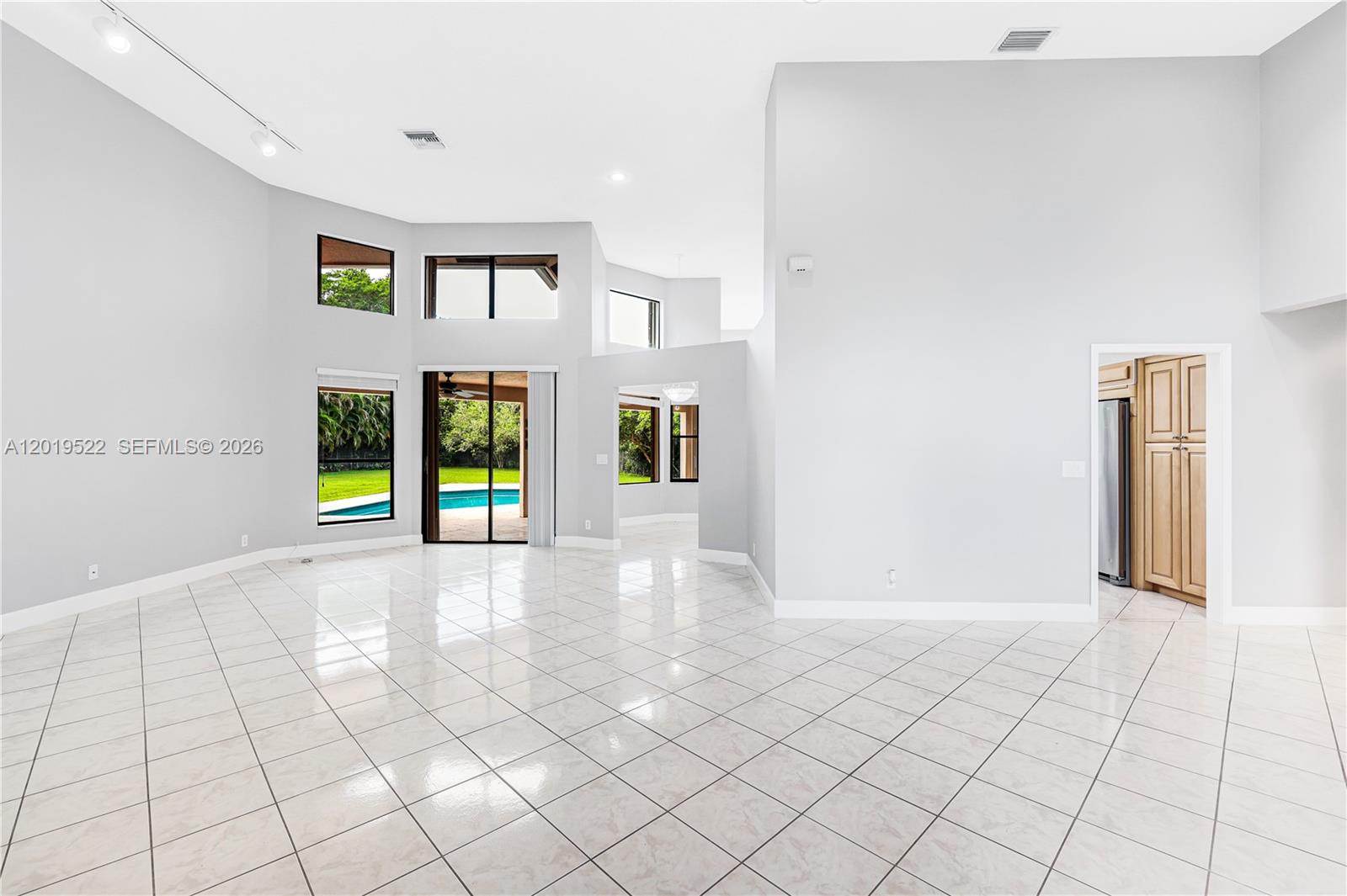 A spacious, high-ceilinged living area features white tile flooring and large windows overlooking a pool — 1256 S Manor Dr S, Weston FL 33326, WESTON, FL
