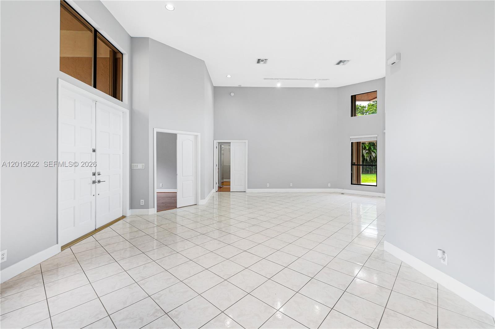 A spacious, high-ceilinged living room features white tile flooring, light gray walls, and double doors — 1256 S Manor Dr S, Weston FL 33326, WESTON, FL