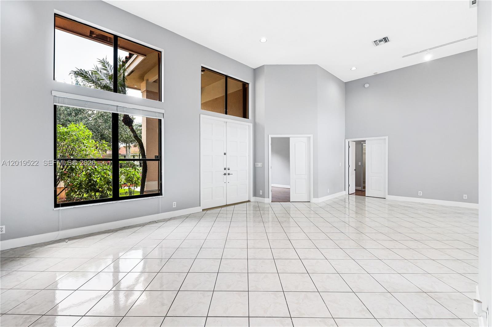 A spacious, high-ceilinged room features white tile flooring, gray walls, and large windows — 1256 S Manor Dr S, Weston FL 33326, WESTON, FL