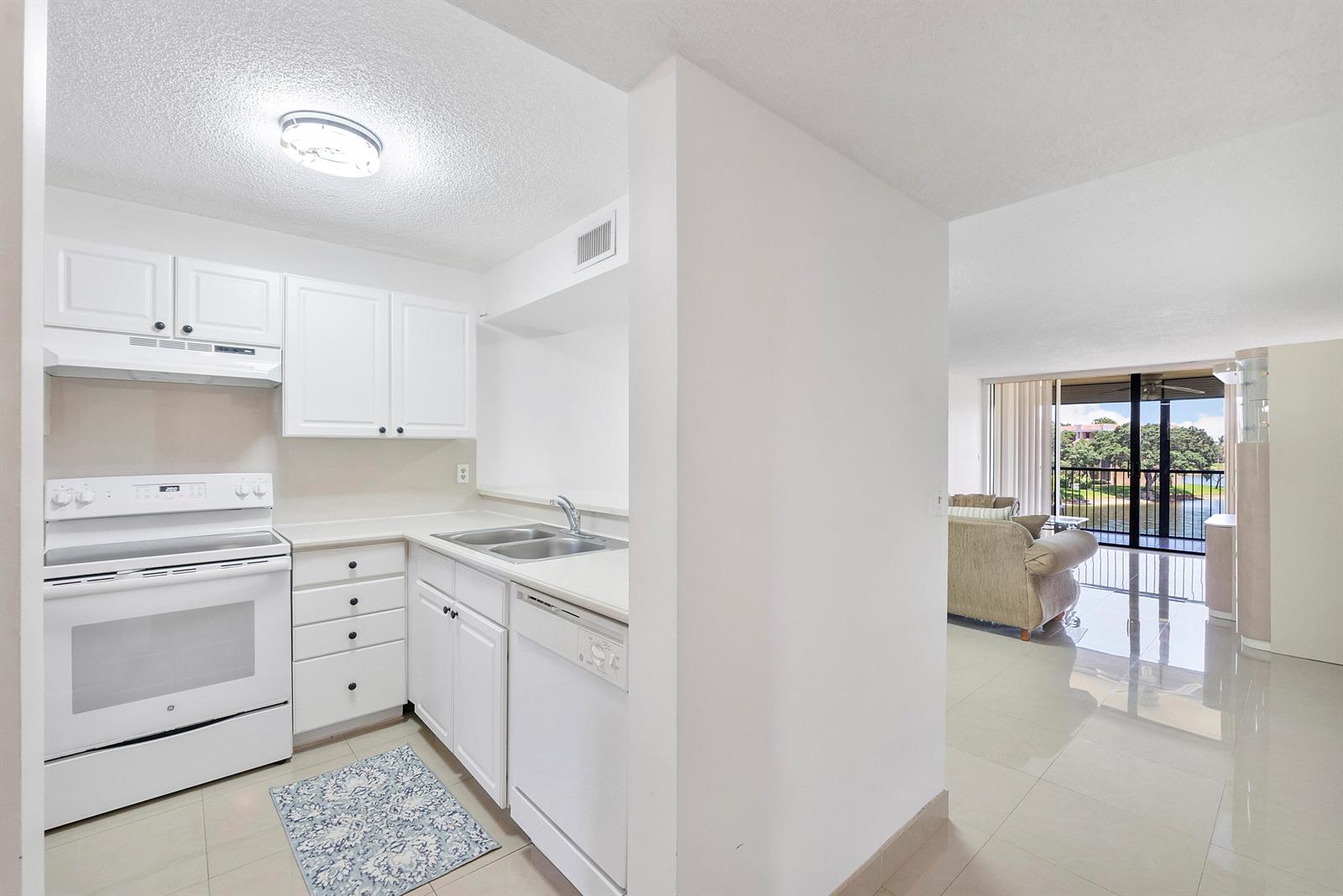 A white kitchen with a stove and dishwasher opens into a bright living room area — 5828 Coral Lake Drive, Margate FL 33063, MARGATE, FL