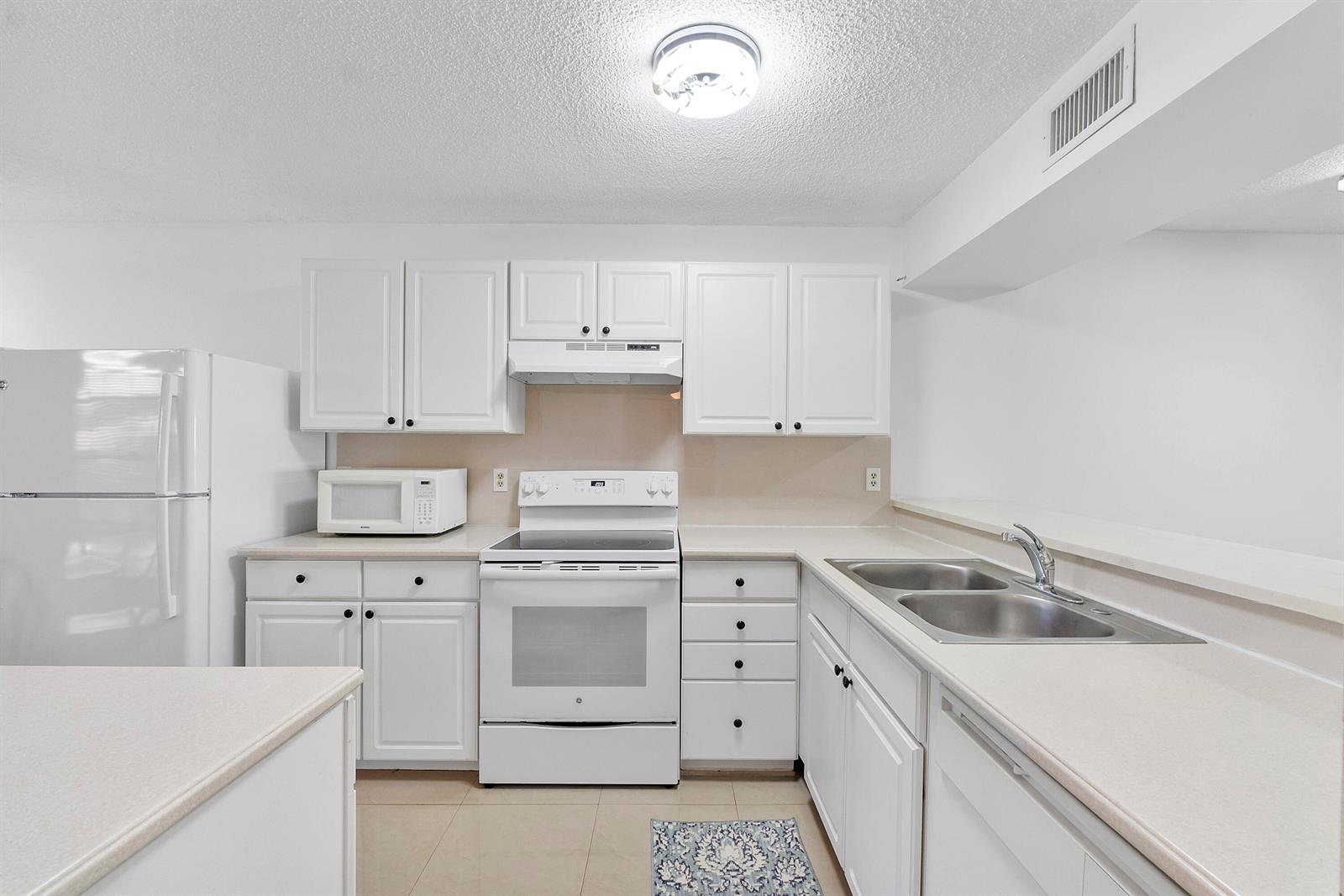 A kitchen features white cabinets, white appliances, a double sink, and light-colored countertops — 5828 Coral Lake Drive, Margate FL 33063, MARGATE, FL