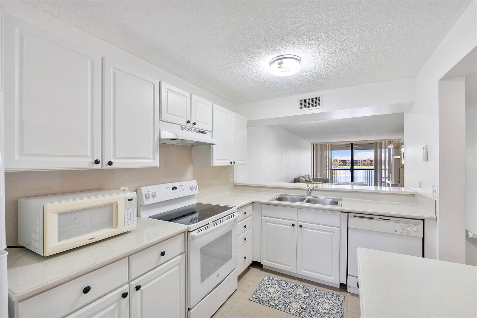 A white kitchen features a stove, dishwasher, microwave, and a view of a lake outside — 5828 Coral Lake Drive, Margate FL 33063, MARGATE, FL