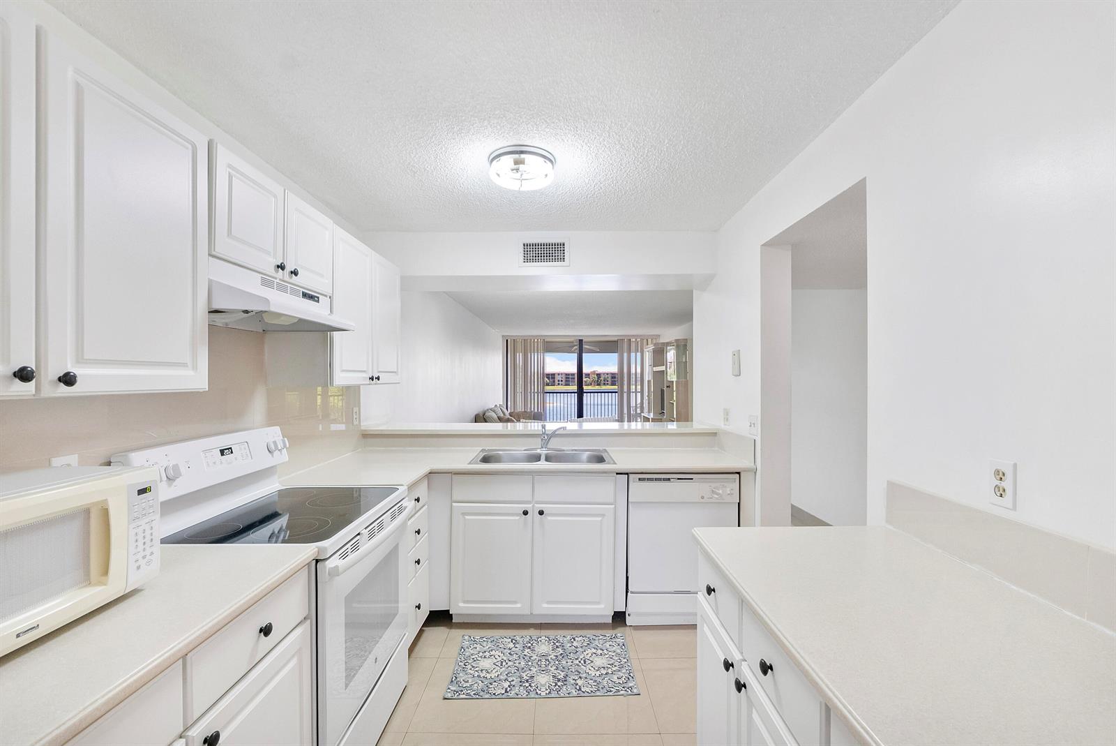 A white kitchen features white cabinets, laminate countertops, and a view of a lake outside — 5828 Coral Lake Drive, Margate FL 33063, MARGATE, FL