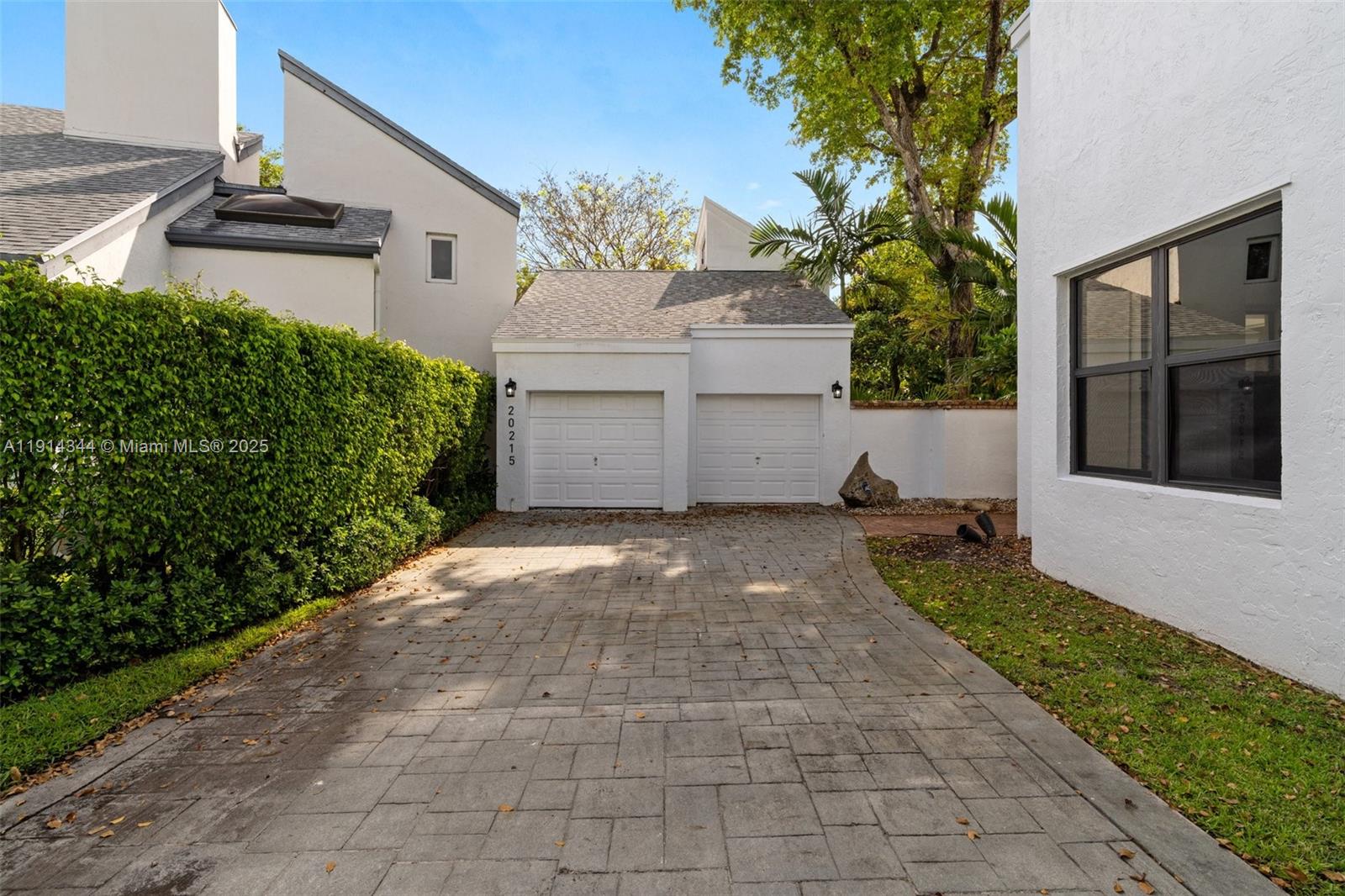 A paved driveway leads to a two-car garage with white doors and a stone wall — 20215 W Oak Haven Cir, Miami FL 33179, MIAMI, FL
