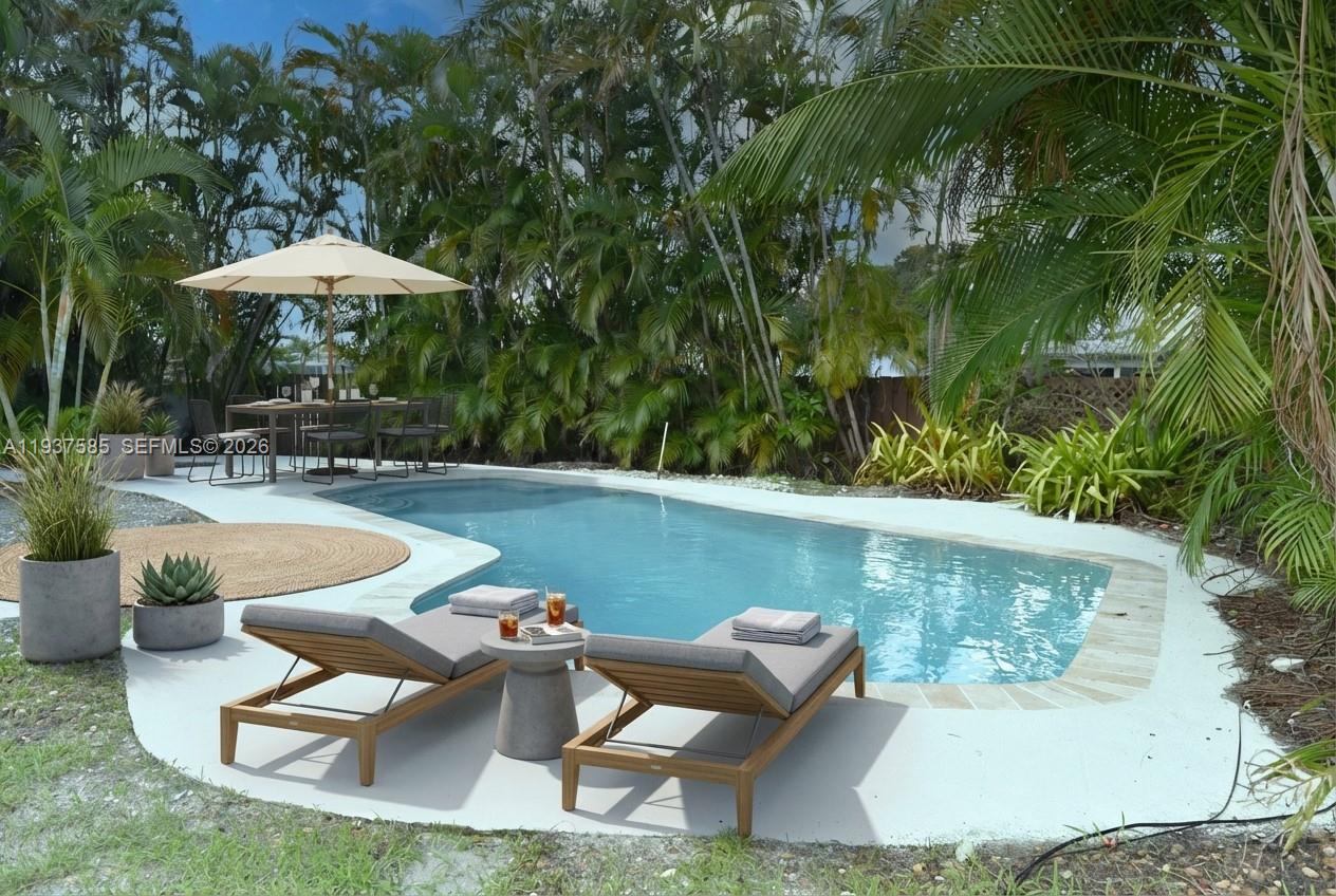 A backyard swimming pool features two lounge chairs, a dining set, and lush tropical landscaping — 4501 Jefferson St, Hollywood FL 33021, HOLLYWOOD, FL