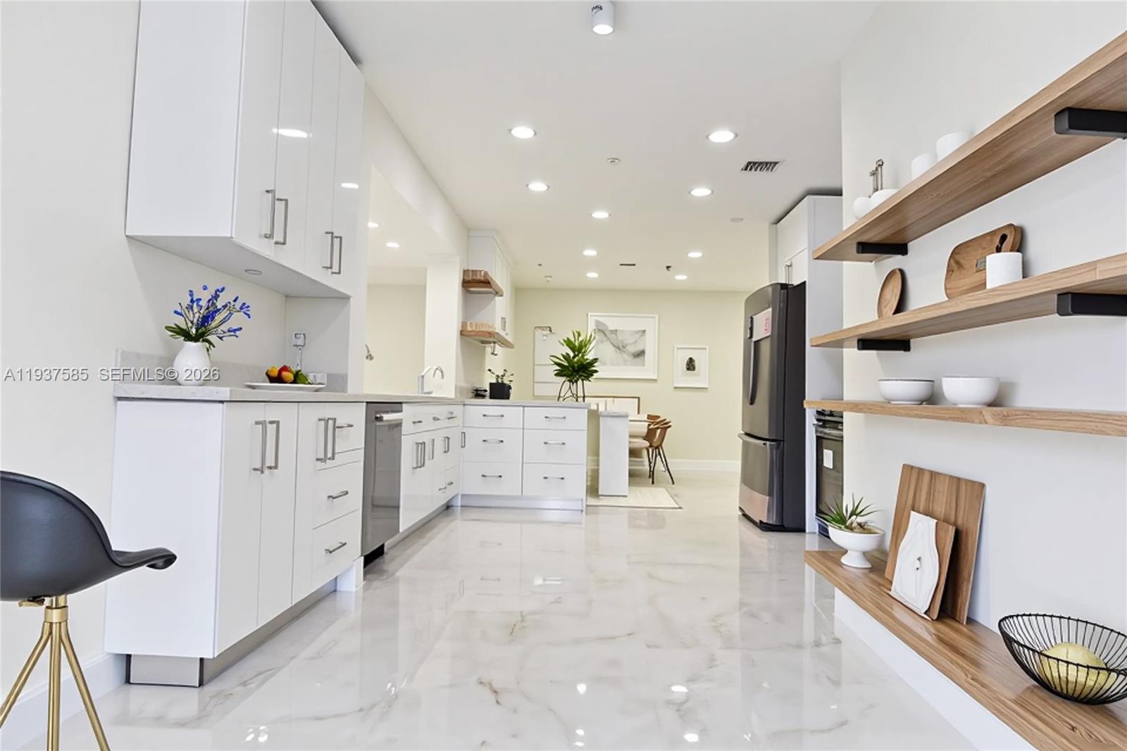 A modern kitchen features white cabinetry, marble-look flooring, and open wooden shelving on the wall — 4501 Jefferson St, Hollywood FL 33021, HOLLYWOOD, FL
