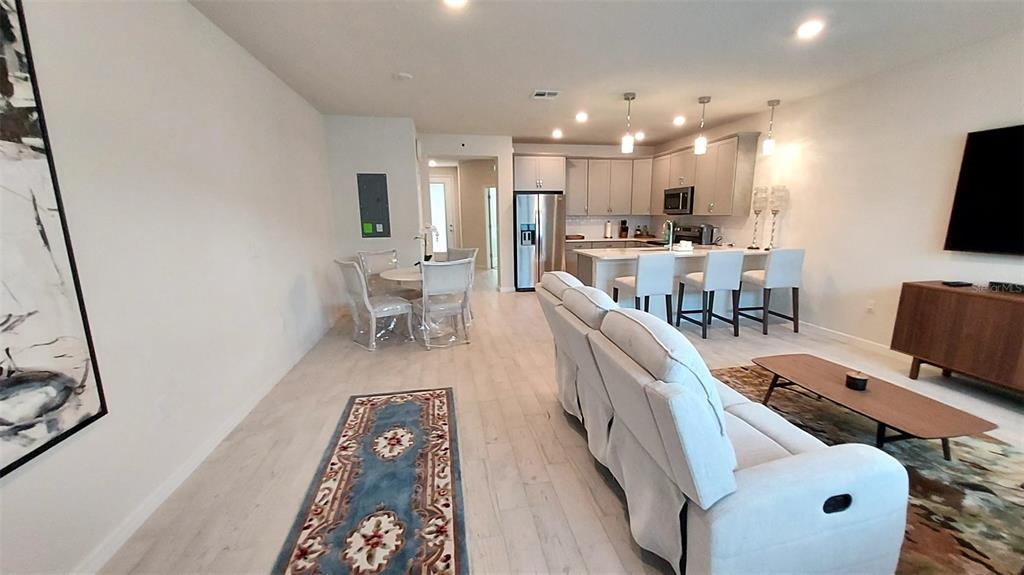 An open-concept living and dining area features light wood floors, neutral walls, and a kitchen — 14169 LANIKAI BEACH DRIVE, ORLANDO, FL