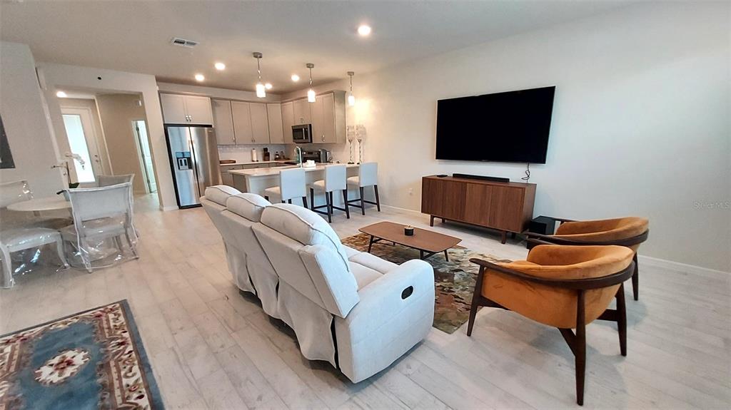 An open-concept living room and kitchen feature light wood flooring, modern furniture, and recessed lighting — 14169 LANIKAI BEACH DRIVE, ORLANDO, FL