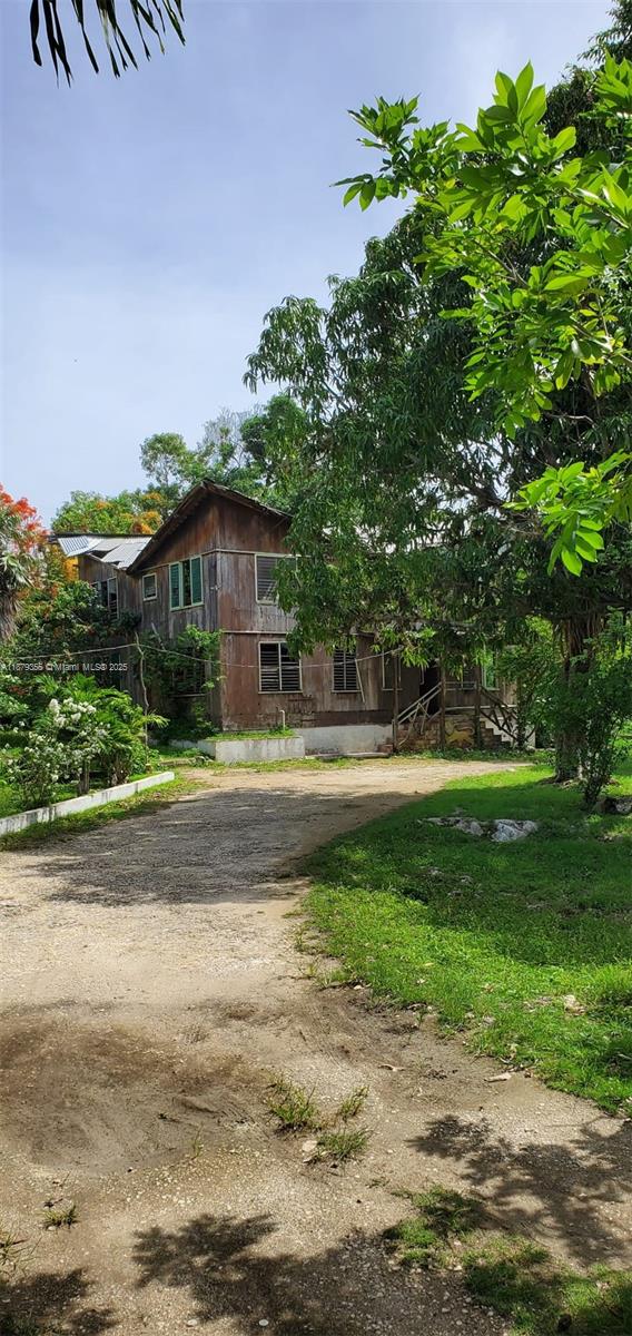 A two-story wooden house with a gravel driveway sits surrounded by lush green trees — 00 West end, Negril Jamaica, NA, NA