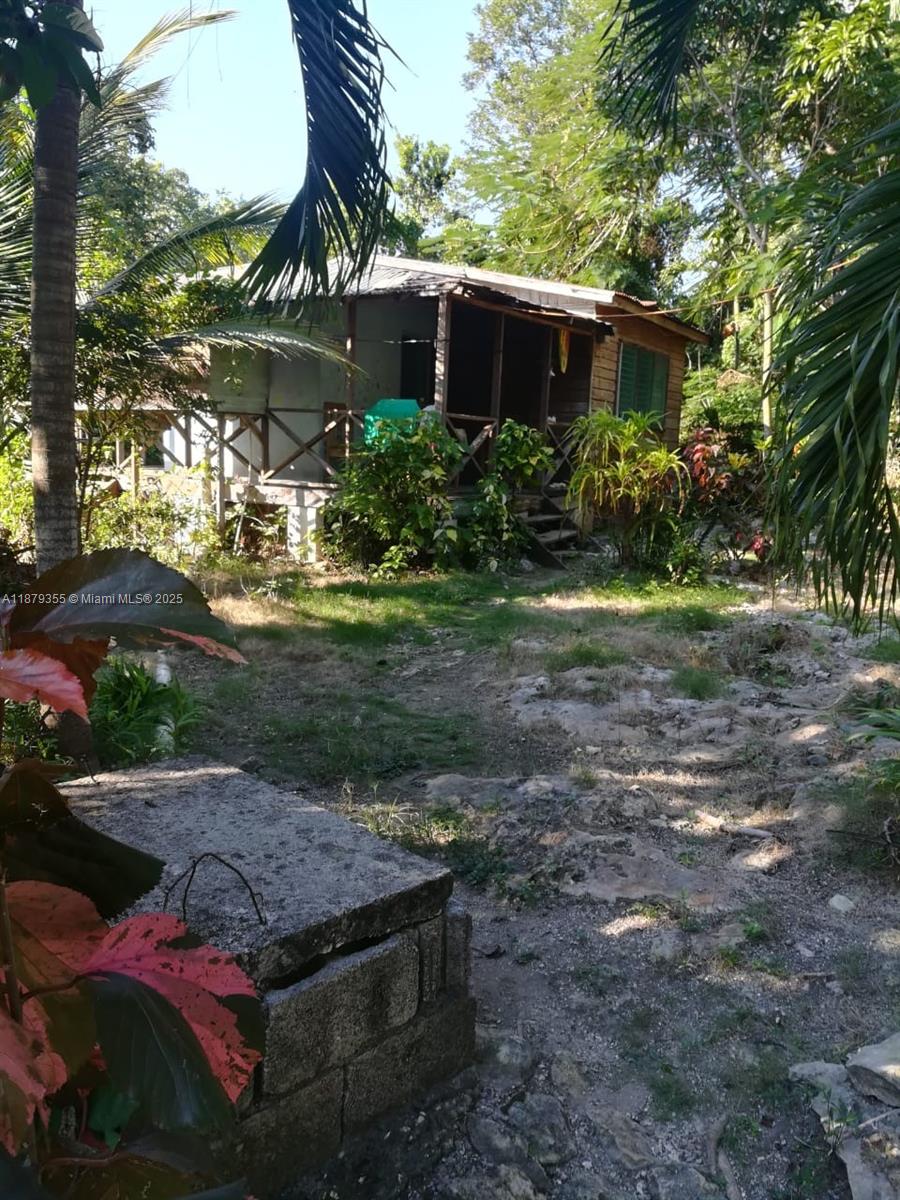 A weathered wooden house with a porch stands in a yard with trees and rocks — 00 West end, Negril Jamaica, NA, NA