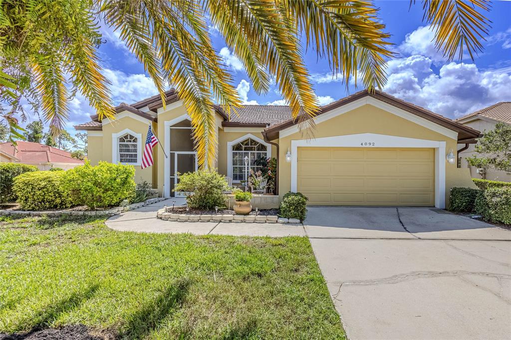 A single-story yellow house with a two-car garage and a palm tree in the front — 4092 HEARTHSTONE DRIVE, SARASOTA, FL