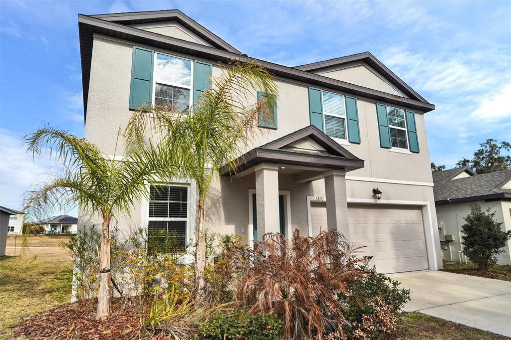 A two-story suburban house with a beige stucco exterior, teal shutters, and a front palm tree — 6803 BRANHAM MILL COURT, ZEPHYRHILLS, FL