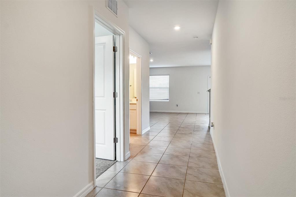 A tiled hallway leads to an open living area with a window and recessed lighting — 6803 BRANHAM MILL COURT, ZEPHYRHILLS, FL