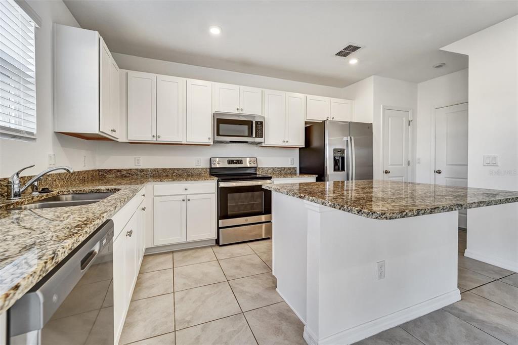 A kitchen features white cabinets, granite countertops, stainless steel appliances, and light tile flooring — 6803 BRANHAM MILL COURT, ZEPHYRHILLS, FL