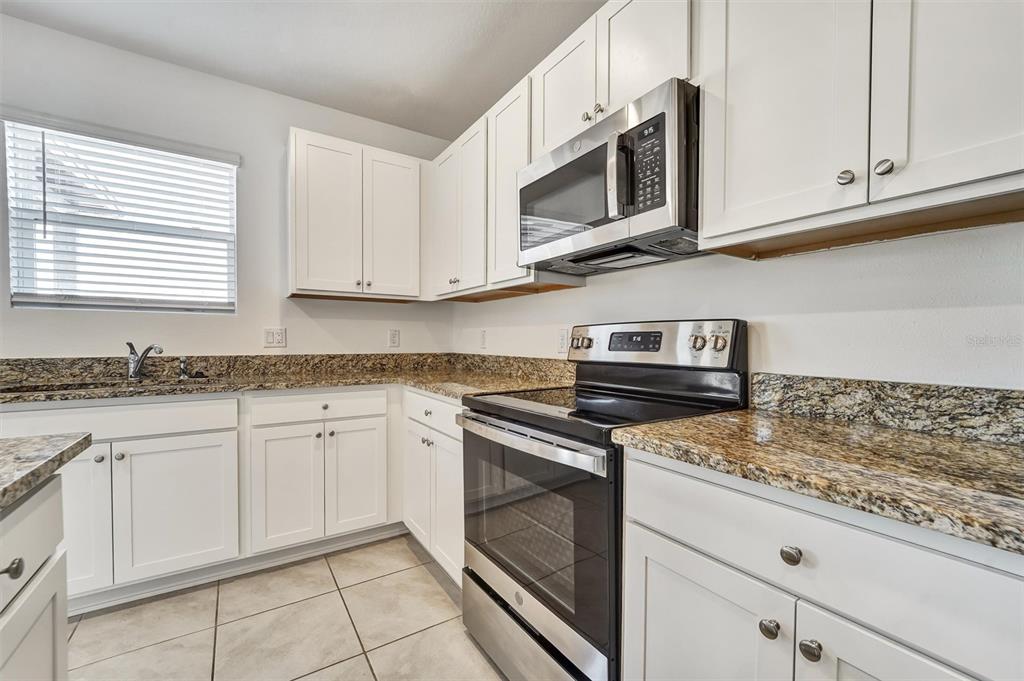 A kitchen with white cabinets, granite countertops, stainless steel appliances, and tile flooring — 6803 BRANHAM MILL COURT, ZEPHYRHILLS, FL